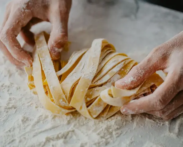 Mani infarinate lavorano un nido di tagliatelle fatte in casa, pronte per essere cucinate.
