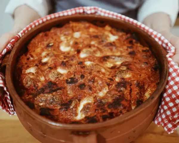 Un invitante pasta al forno ricetta della nonna, appena sfornata in una terracotta, con crosticina dorata e ripieno filante.
