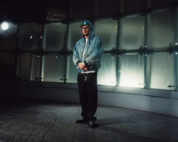 Pezet w niebieskiej kurtce i czapce z daszkiem, stojący w nowoczesnym, przeszklonym wnętrzu. To jego plan B na wieczór.