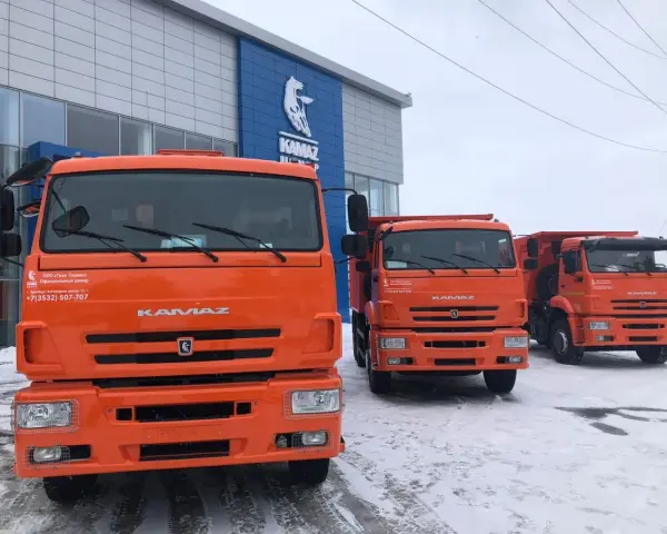 Trzy pomarańczowe, rosyjskie ciężarówki KAMAZ stoją przed budynkiem dealera.