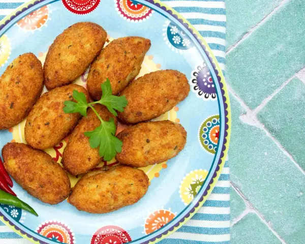 Croquetas doradas en un plato decorado con pimientos y perejil.