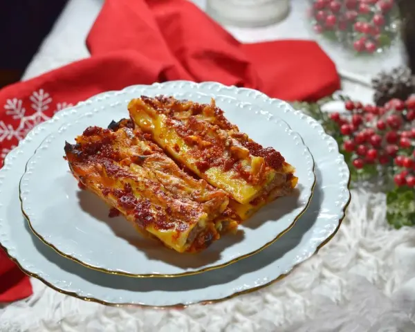 Due cannelloni di carne fumanti, ricoperti di sugo rosso e formaggio filante, serviti su un piatto bianco con bordo dorato, pronti per essere gustati.