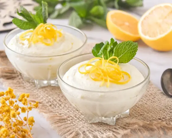 Dos copas de cremoso mousse de limón con leche condensada, decoradas con ralladura de limón y menta.