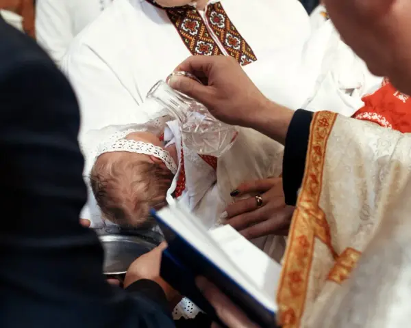 Ceremonia chrztu dziecka. Duchowny polewa główkę niemowlęcia wodą święconą. Warto wiedzieć, ile kosztuje chrzest.