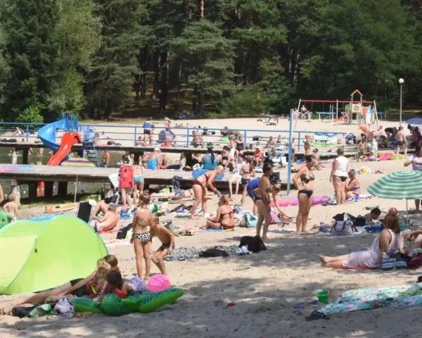 Tłoczna plaża nad jednym z **jezior blisko Wrocławia**. Ludzie opalają się, kąpią i odpoczywają na piasku.