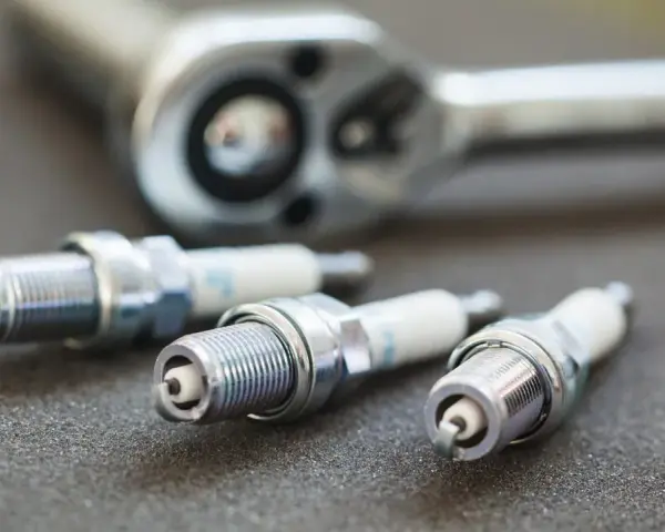 Three spark plugs and a ratchet are laid out, ready for a tune-up. The image highlights the importance of knowing the correct spark plug socket size for the job.
