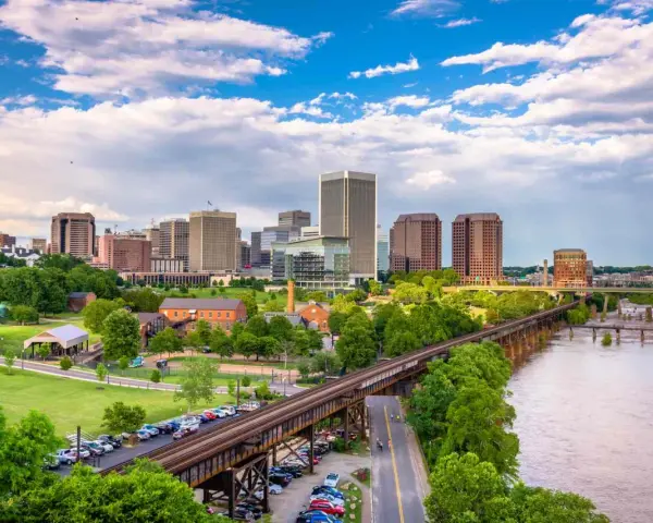 A scenic view of Richmond, VA, showcasing the city skyline, a river, and a railway bridge. Perfect for a weekend getaway.