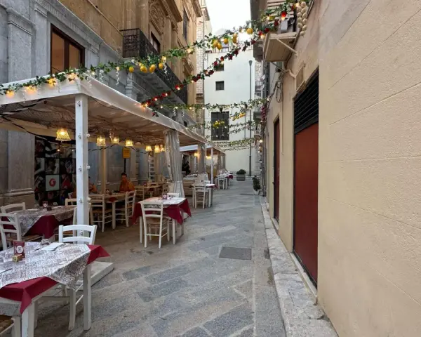 Urocza uliczka w Trapani, gdzie zjeść? Stoliki restauracyjne pod girlandami z cytryn i lampek, idealne na wieczorny posiłek.