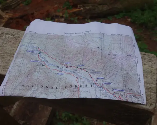 Mapa szlaku grzbietu pacyficznego z zaznaczonymi punktami i rzekami, leżąca na drewnianej ławce.