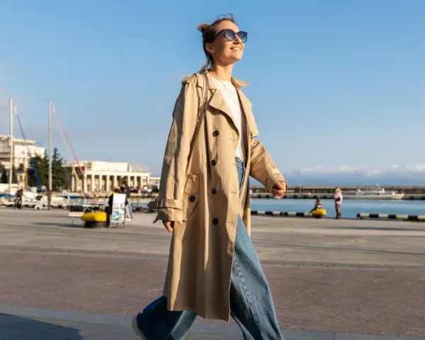 Una chica con estilo, con un look clean girl, pasea por el puerto con un abrigo beige y vaqueros anchos.