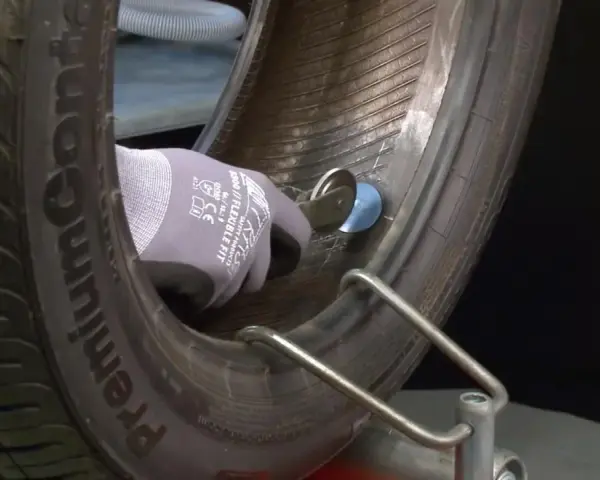 Mano guantata che esegue la riparazione gomma con un attrezzo, fissando una toppa interna.