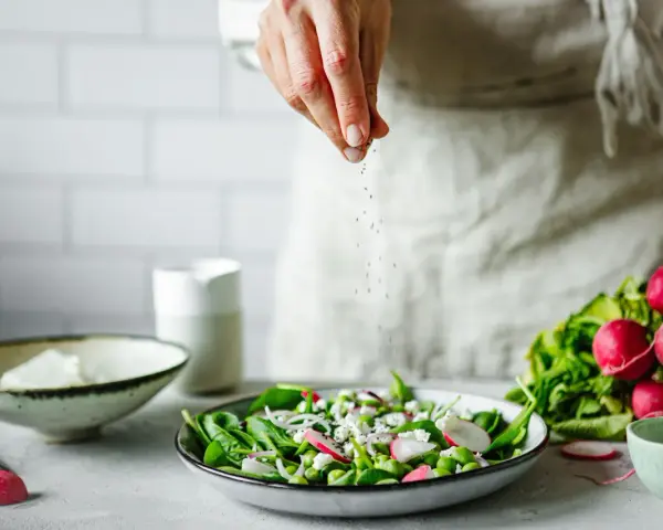 Une main saupoudre des graines sur une salade fraîche. Une idée pour une recette de radis noir.