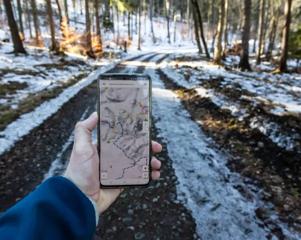 Telefon z mapą pokazuje szlak w lesie. Widać ślady śniegu na drodze, a na ekranie zaznaczony jest skopiec szlak.