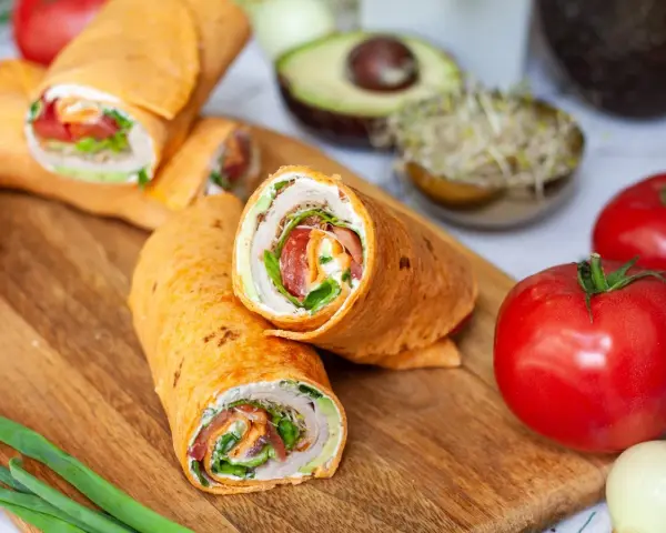 Pyszna tortilla na śniadanie z warzywami i kremowym serkiem. Obok pomidory, awokado i kiełki.