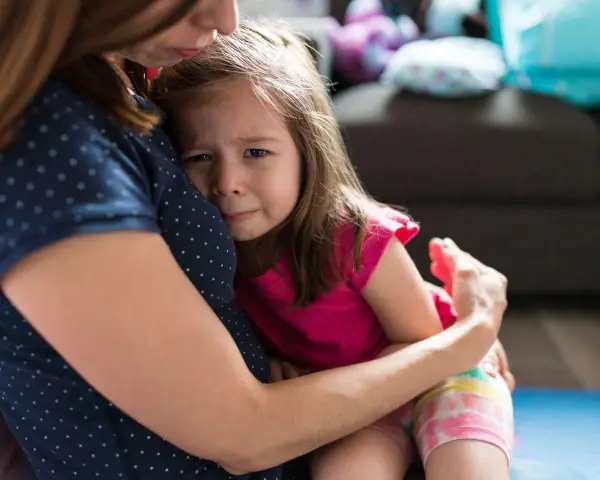 Mała dziewczynka płacze, wtulona w mamę. To właśnie parenting – trudne chwile i bezwarunkowa miłość.