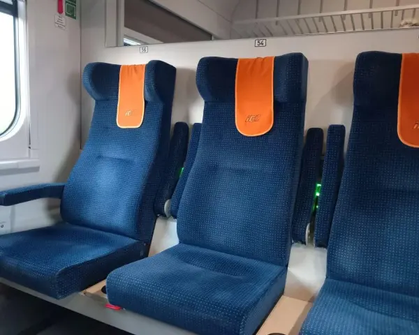 Komfortowe siedzenia w pociągu do Giżycka. Pomarańczowe zagłówki z logo PKP dodają koloru.