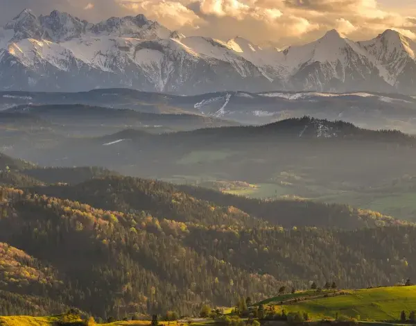 Złote światło oświetla najpiękniejsze szczyty w Polsce, Tatry, otoczone przez malownicze, zalesione wzgórza.