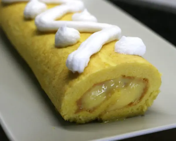 Un brazo de gitano amarillo con relleno cremoso y merengue blanco decorando la superficie.