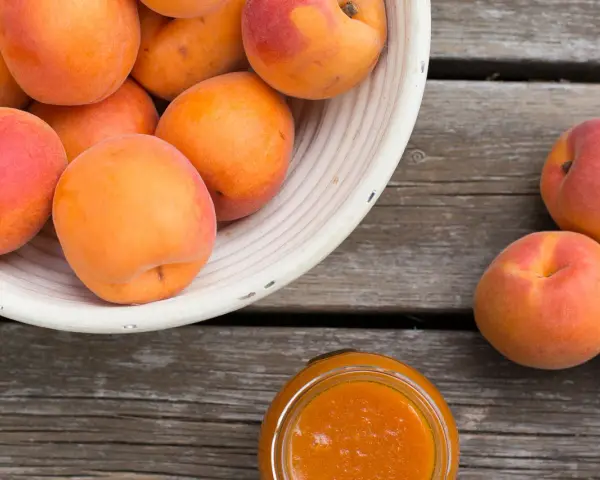 Ein Korb voller reifer Marillen, daneben ein Glas Marillenmarmelade. Was sind Marillen? Süße Früchte, perfekt für Marmelade!