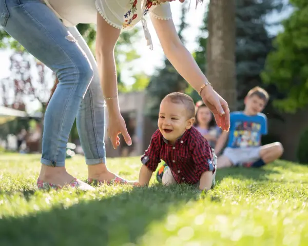Uśmiechnięte dziecko raczkuje na trawie, podczas gdy opiekunka zastanawia się, ile kosztuje niania na pełen etat.