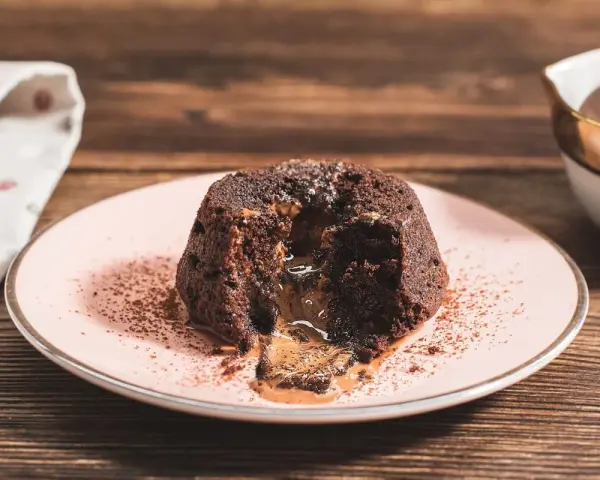 Coulant de chocolate con centro líquido y cremoso, espolvoreado con cacao en polvo sobre un plato rosa.