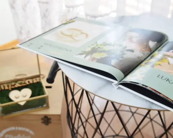 Elegancka szkatułka na obrączki i otwarty album ślubny z imionami Magdaleny i Łukasza. Idealne inspiracje, co zabrać na wesele jako gość.