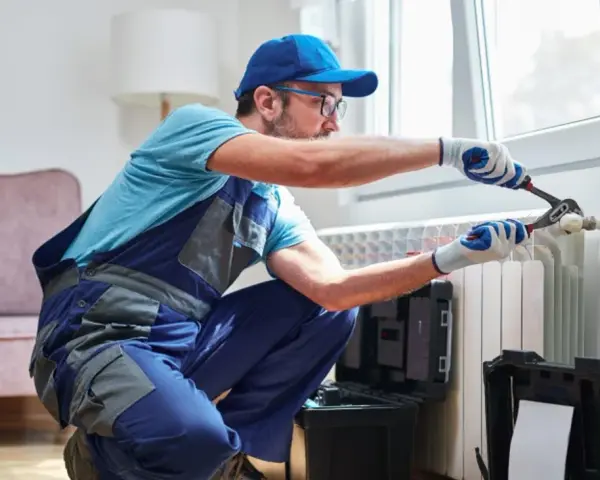 Tecnico con attrezzi effettua manutenzione termosifoni vicino a una finestra.