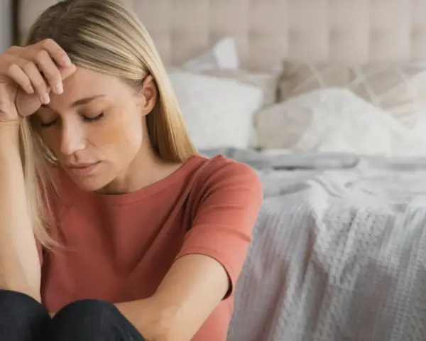 Kvinna med slutna ögon, handen mot pannan. Kanske en känsla av depression under klimakteriet, men det finns behandling.