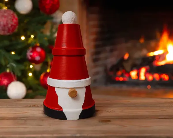 En söt tomte gjord av krukor står framför en sprakande brasa och en julgran. Perfekt för att måla tomte-pyssel.