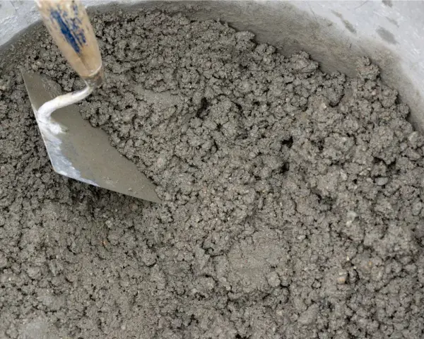 Una cazzuola mescola la malta appena preparata in un secchio. Ecco come fare la malta per i tuoi progetti.