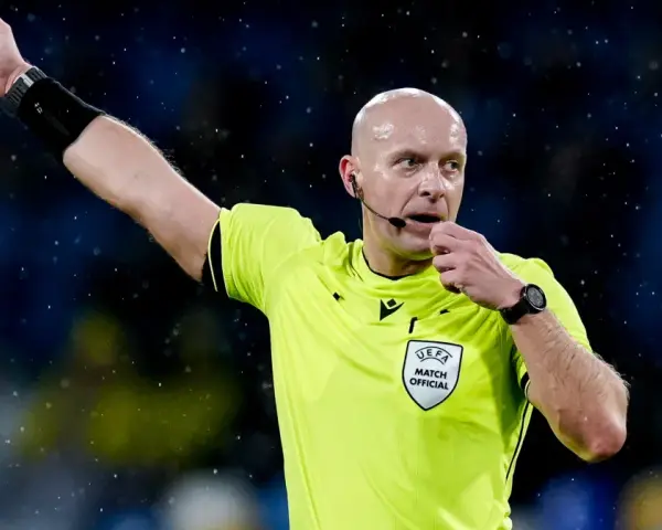 Sędzia piłkarski w żółtej koszulce z naszywką UEFA, dmucha w gwizdek. Zastanawiasz się, ile zarabia sędzia piłkarski?