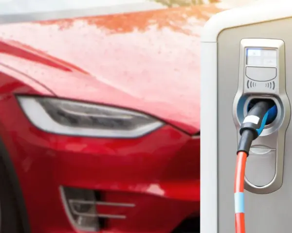 Czerwona Tesla podłączona do ładowarki. Czas ładowania zależy od modelu i mocy stacji.
