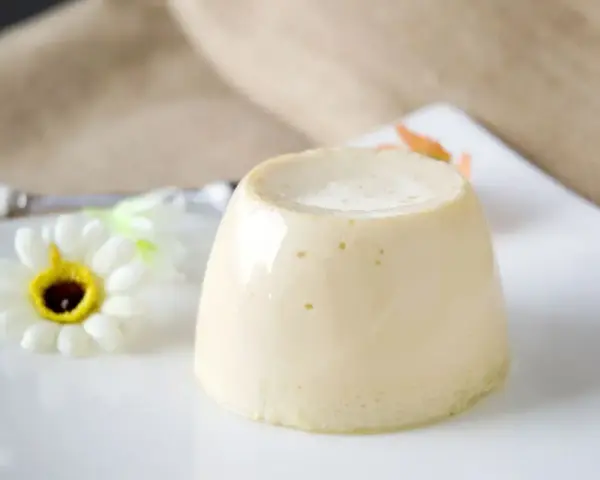 Delizioso budino fatto in casa, servito su un piatto bianco con un fiore decorativo.