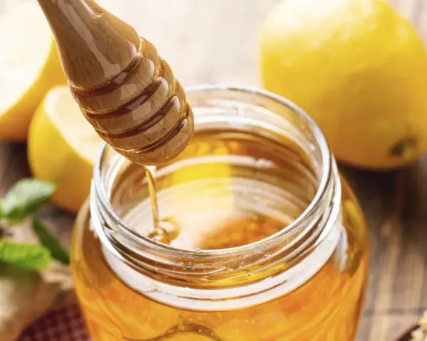 Un pot de miel doré, des citrons et de la menthe, évoquant le bienfait du miel sur la peau.