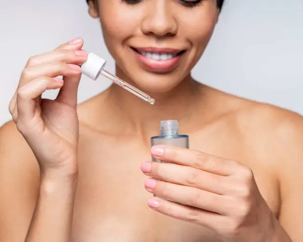 Une femme souriante applique un sérum. Elle se demande combien de temps entre sérum et crème pour une peau parfaite.