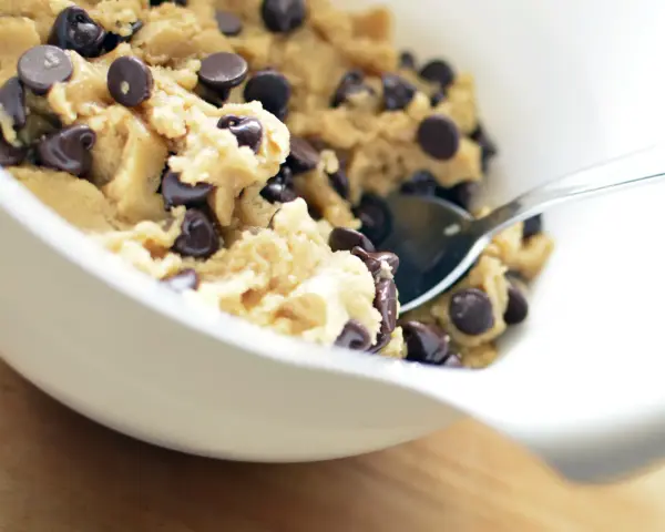 En skål med ljuvlig cookie dough med chokladbitar, redo för ett enkelt cookie dough recept. En sked vilar i smeten.