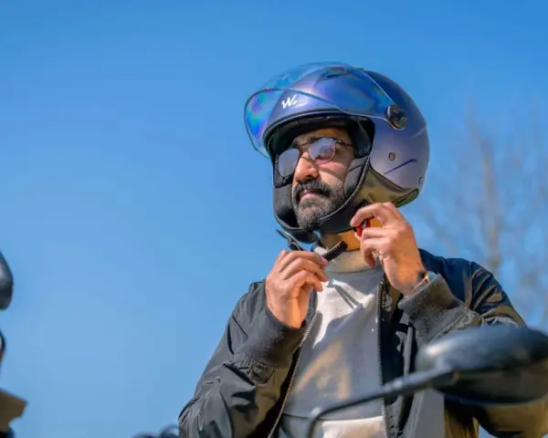 Uomo con barba che indossa un casco da moto blu iridescente, pronto per un giro.
