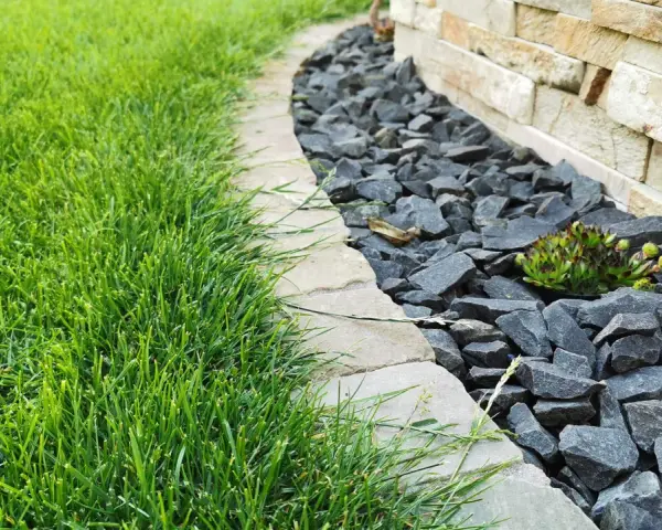 Ein Gartenweg mit frisch gemähten Rasen und grauen Bruchsteinen, die den Rand eines Beetes mit einer Sukkulente markieren. Die Pflastersteine schneiden eine klare Linie.