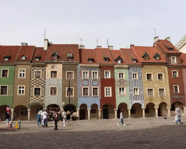 Kolorowe kamienice na Starym Rynku w Poznaniu, wspaniałe poznan atrakcje. Ludzie spacerują po brukowanym placu.