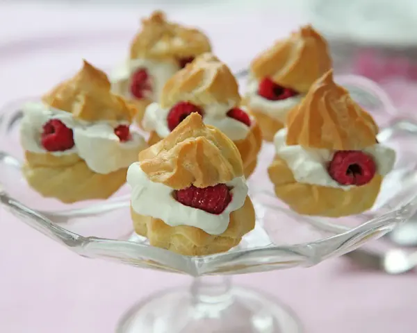 Små petit choux fyllda med grädde och hallon på ett glasfat.