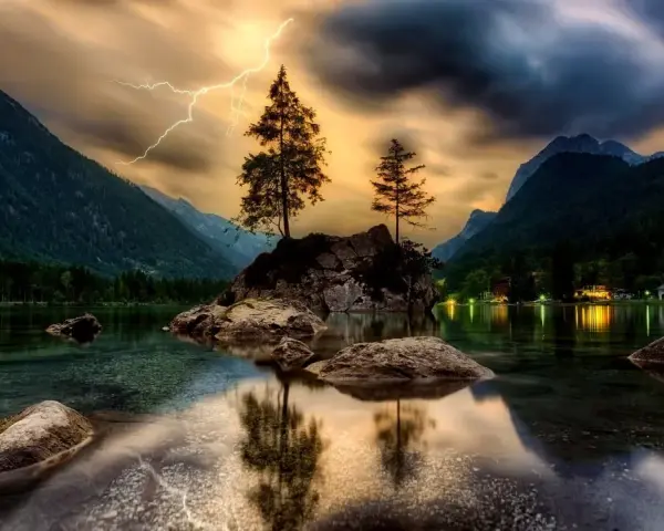 Dramatyczne zdjecia hdr: błyskawica nad skalistą wyspą z drzewami na środku jeziora, otoczonego górami.
