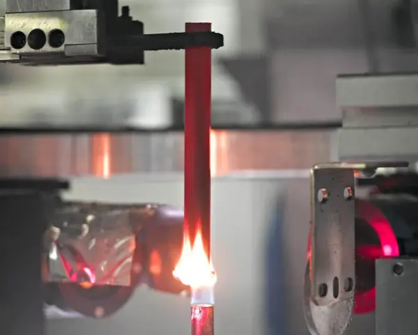A red acrylic rod is tested for how acrylic fire resistant it is, with a flame licking its base.