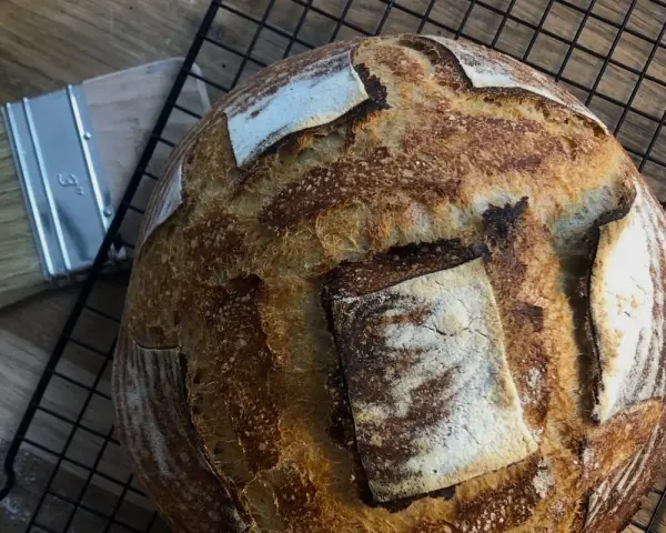 Chleb pszenno żytni na zakwasie, pachnący świeżością, czeka na ostygnięcie. Obok pędzel do pieczenia.