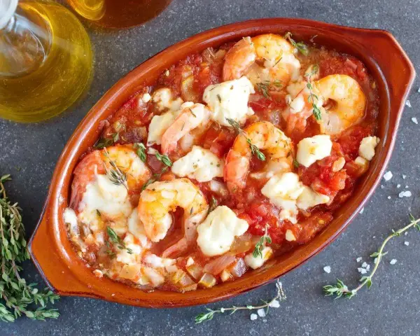 Gamberoni al guazzetto in terracotta, con pomodoro, formaggio fuso e timo. Un piatto invitante pronto per essere gustato.