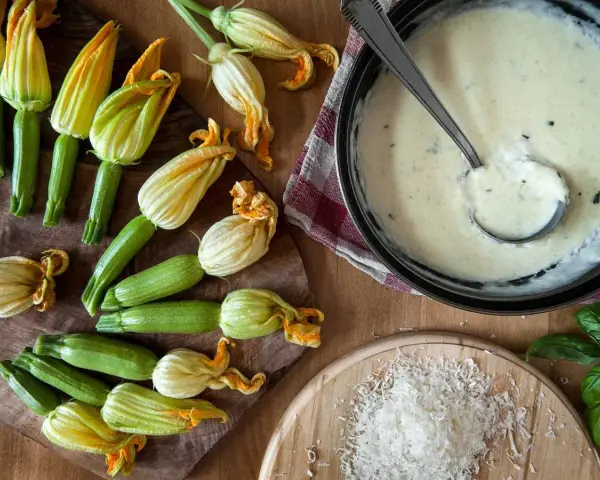 Flores de calabacín frescas y una salsa cremosa en una sartén.
