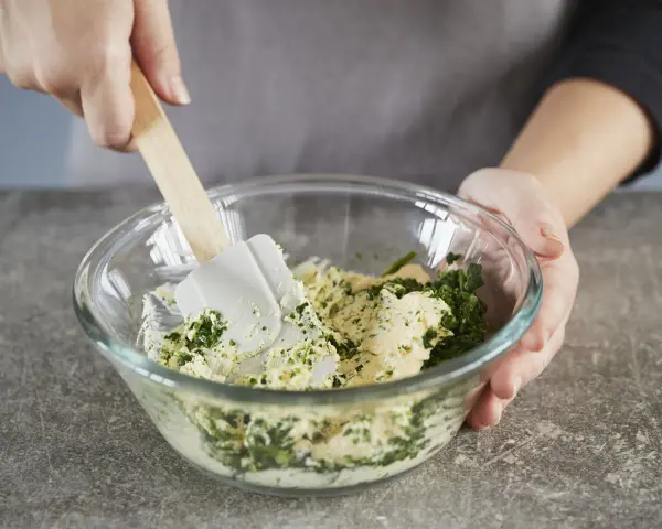 Hände mischen Kräuter und Butter in einer Schüssel. Perfekt, um Kräuterbutter selber zu machen.