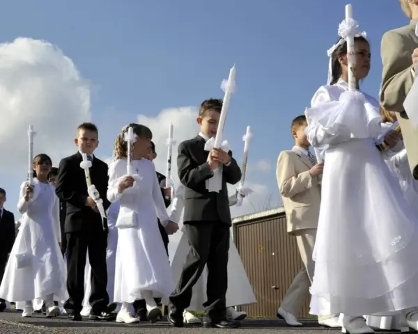 Kinder in festlicher Kleidung, was zieht man zur Kommunion an? Mädchen in weißen Kleidern, Jungen in Anzügen, alle tragen Kerzen.