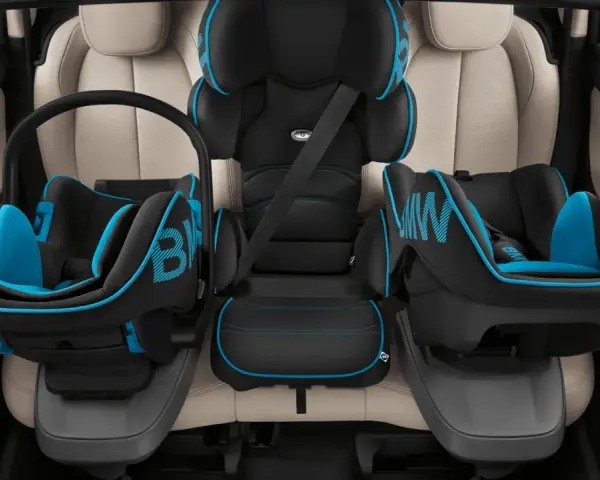 Trois sièges auto pour enfant, noir et bleu, installés sur des sièges en cuir clair. Le transport enfant en voiture est sécurisé.