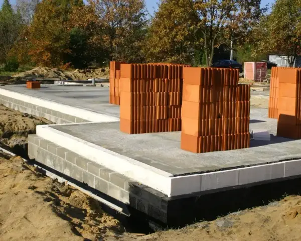Budowa domu: betonowy fundament, bloczki, palety cegieł. Zastanawiasz się, ile kosztują fundamenty? Oto początek inwestycji.