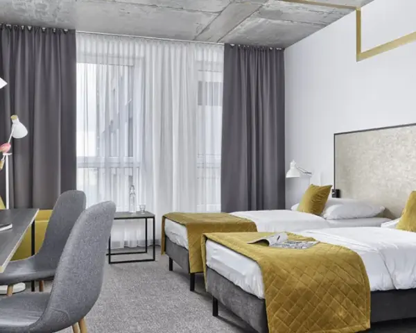 Pokój hotelowy z dwoma łóżkami, biurkiem i kwiatami. Idealne miejsce na wcześniejsze zameldowanie w hotelu.